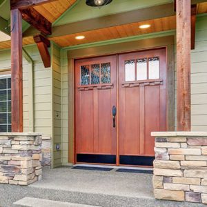product-inset_doubledoor Wooden double entry doors with windows on the top third on the exterior of a greenish house and wood accents.