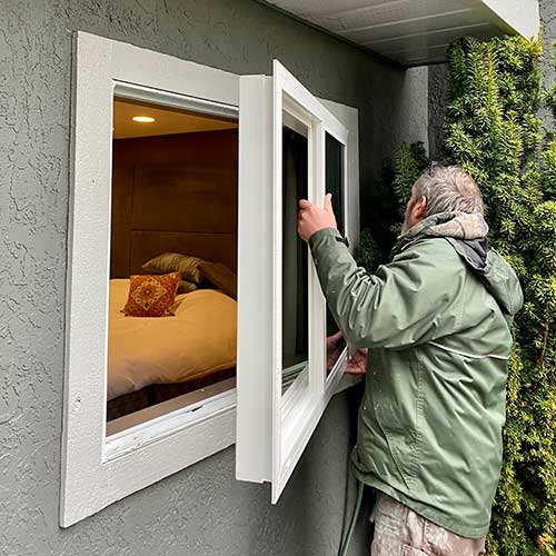 A man installing a window into a house.