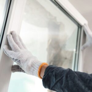 van-isle-windows-window-installation Two hands wearing white gloves installing a white vinyl window frame.
